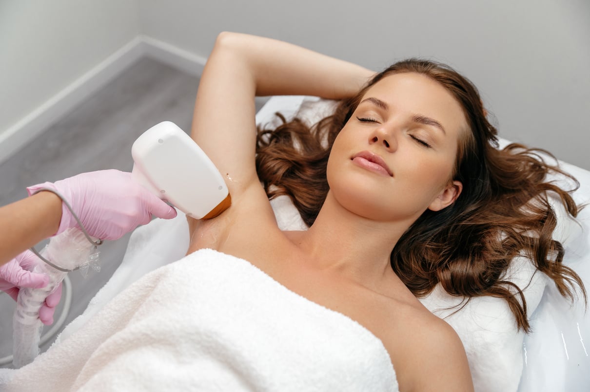 Aesthetic cosmetology. Laser epilation. Caucasian young woman lies on a couch in a beauty salon during laser hair removal of the armpit area